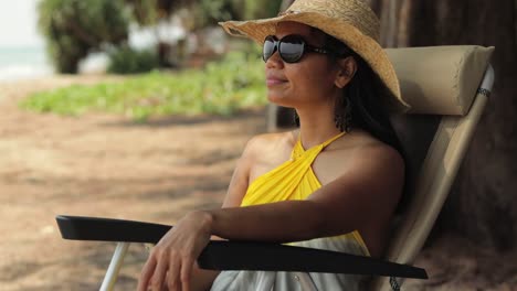 asian woman sitting on a beach chair wearing summer hat