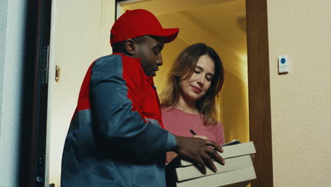 Joven-Con-Uniforme-Y-Gorra-Entregando-Pizza-A-La-Mujer