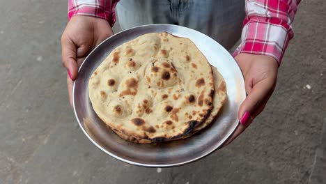 una chica sosteniendo tandoori roti pan plano de trigo entero en una carretera