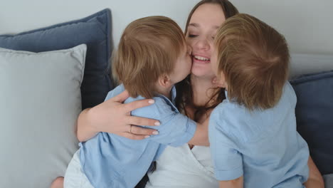 Mom-is-sitting-on-the-couch-with-a-laptop.-Two-boys-children-sing-and-kiss-their-mom