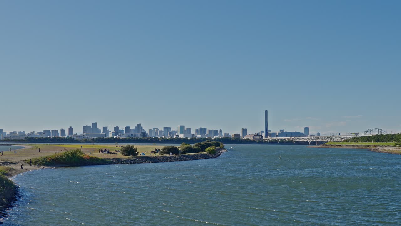 A sweeping view of the distant urban skyline across the water, featuring a tall structure and bridge in the background