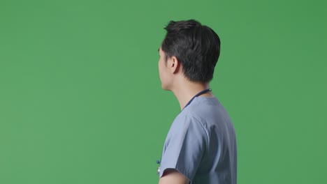 close up of side view asian male doctor with stethoscope looking around and walking on green screen background in the hospital