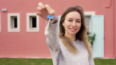 Happy-woman-showing-keys-of-new-apartment-outside-new-home