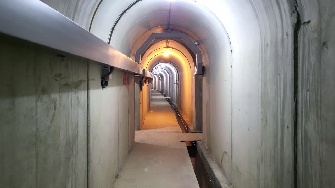 Galleria di ispezione e manutenzione all'interno della diga. Area di manutenzione sotterranea, illuminazione, condotti per cablaggi elettrici e zona di raccolta dell'acqua di drenaggio. Spagna.