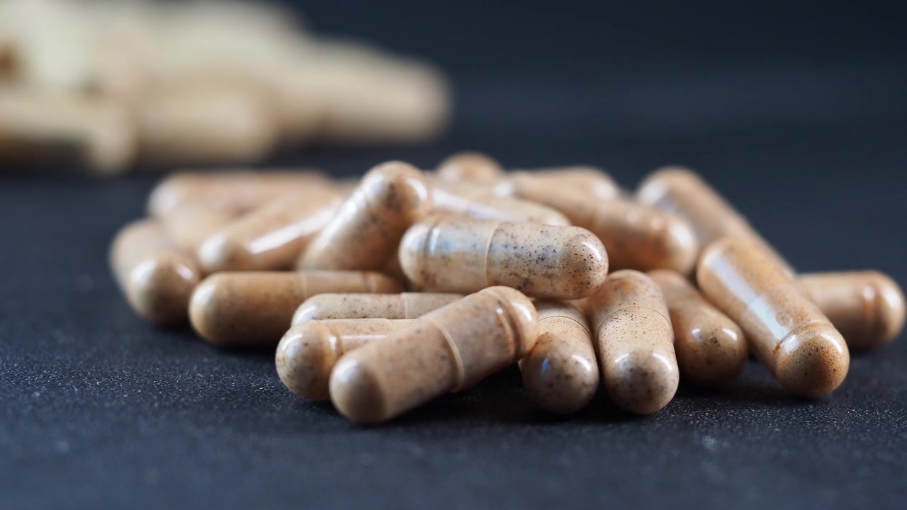 Pila di capsule di integratori erboristici su superficie scura