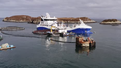 Reversing-drone-shot-of-fishing-boats-docked-to-a-fish-farm-cage-on-Uist