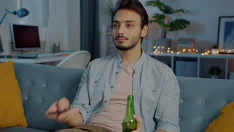 man relaxing on couch, watching tv and drinking beer.