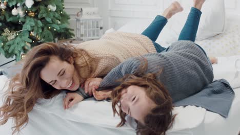 cheerful woman and teen girl hugging each other on double bed.