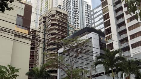 4K-descending-view-of-a-cluster-of-tall,-close-knit-modern-buildings-on-a-famous-avenue-with-tropical-vegetation-in-Panama-City