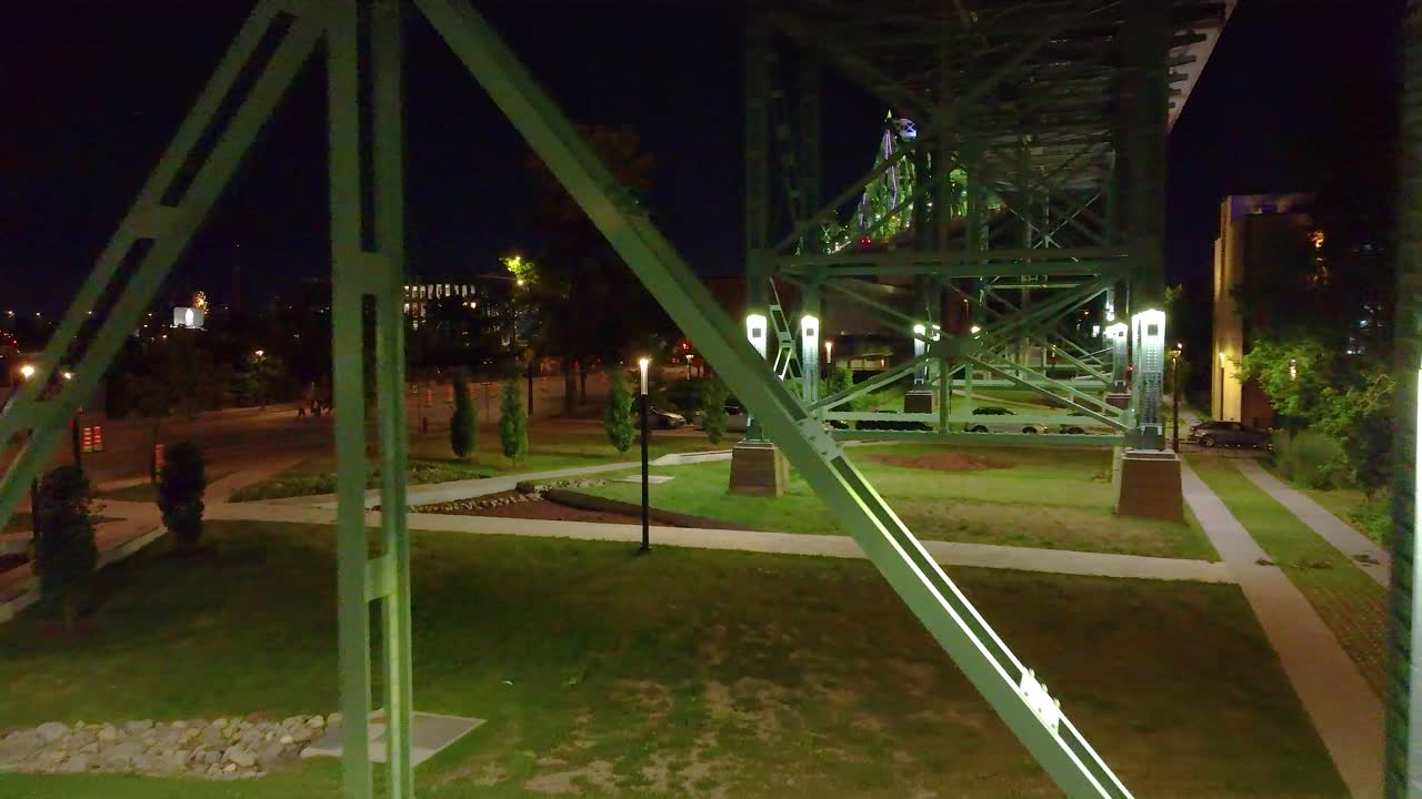 Drone glides between green steel pillars of bridge at night in Montreal, Quebec, Canada.