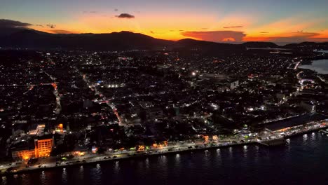 una brillante puesta de sol naranja sobre una calle iluminada ciudad de surigao | filipinas, en una impresionante toma aérea de dron
