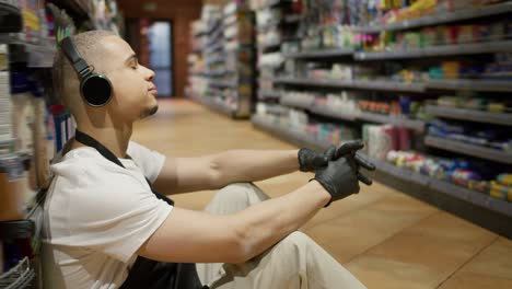 Supermarket-worker-in-apron-sitting-on-the-floor-and-listen-to-the-music