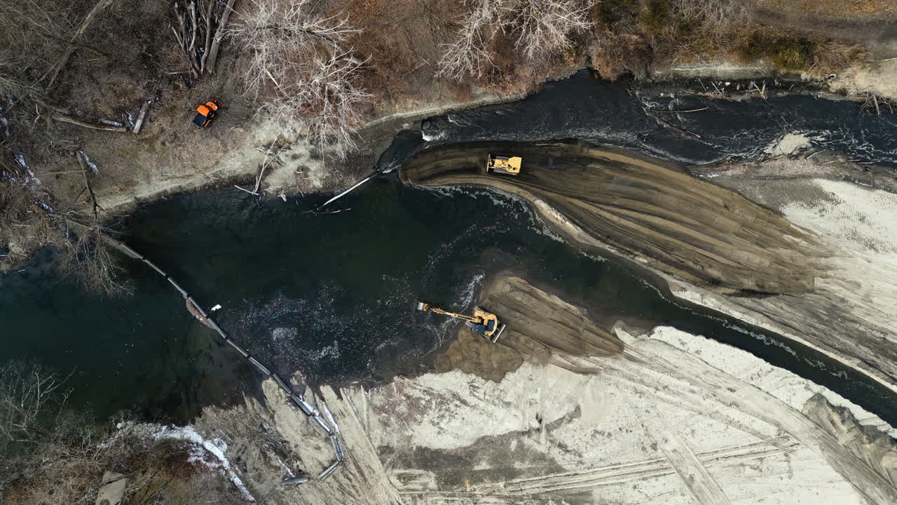 Aerial perspective of bulldozers and excavators altering the direction of a river's flow