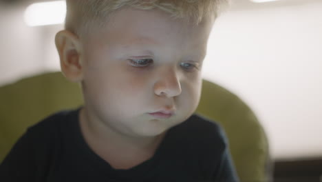 un niño atento con cabello rubio mira hacia adelante en casa