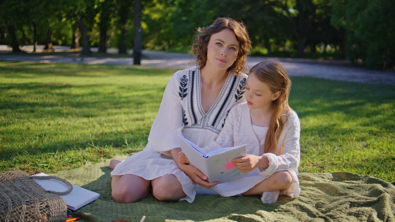 Lezende familie die samen picknickt in een zomerpark. Moeder en dochter houden een boek vast