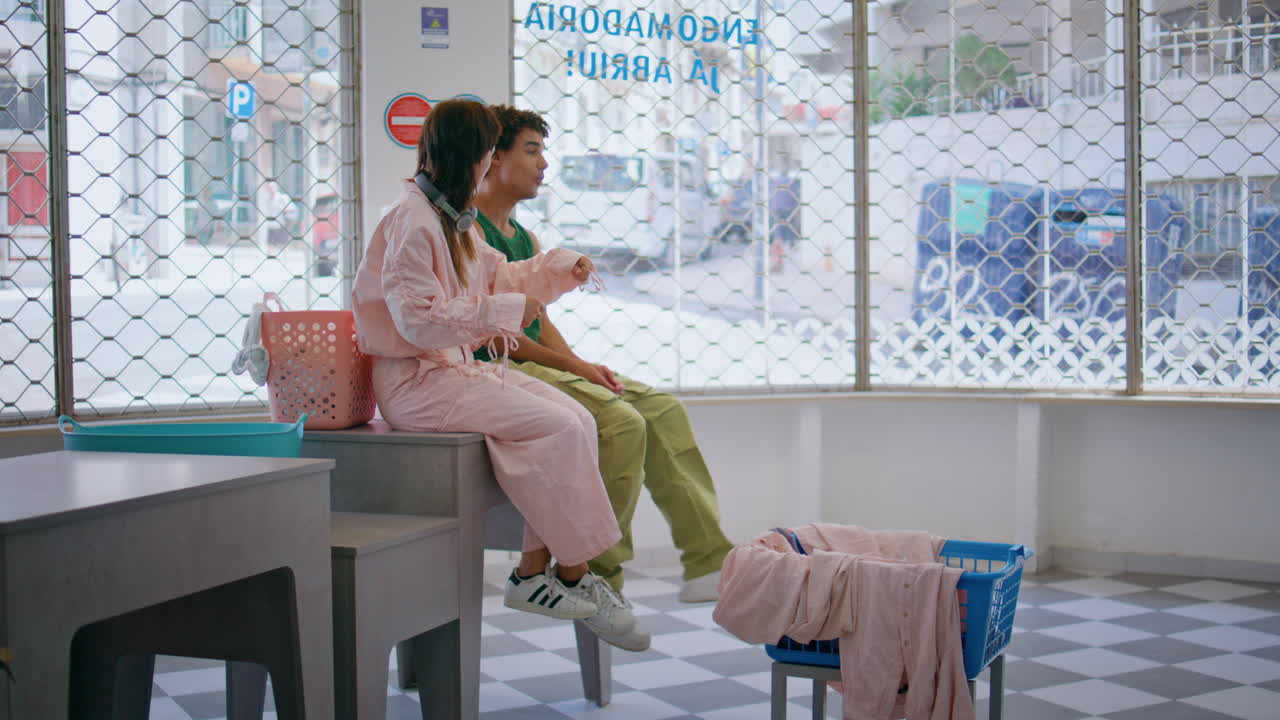 두 친구가 공용 세탁실에서 유혹을 하고 있다. 학생들이 옷을 고 기다리고 있다.