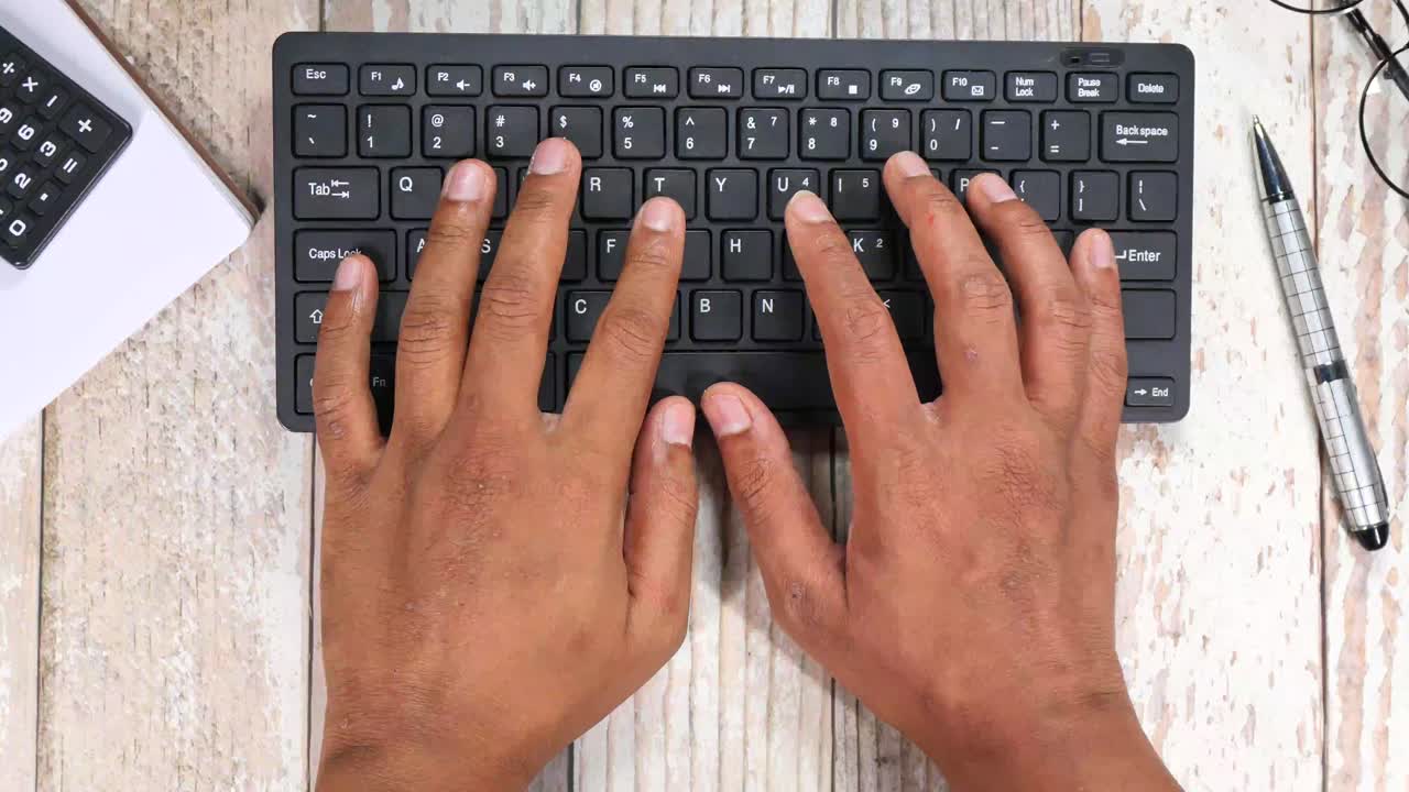 Close-up of hands typing on a keyboard at a desk