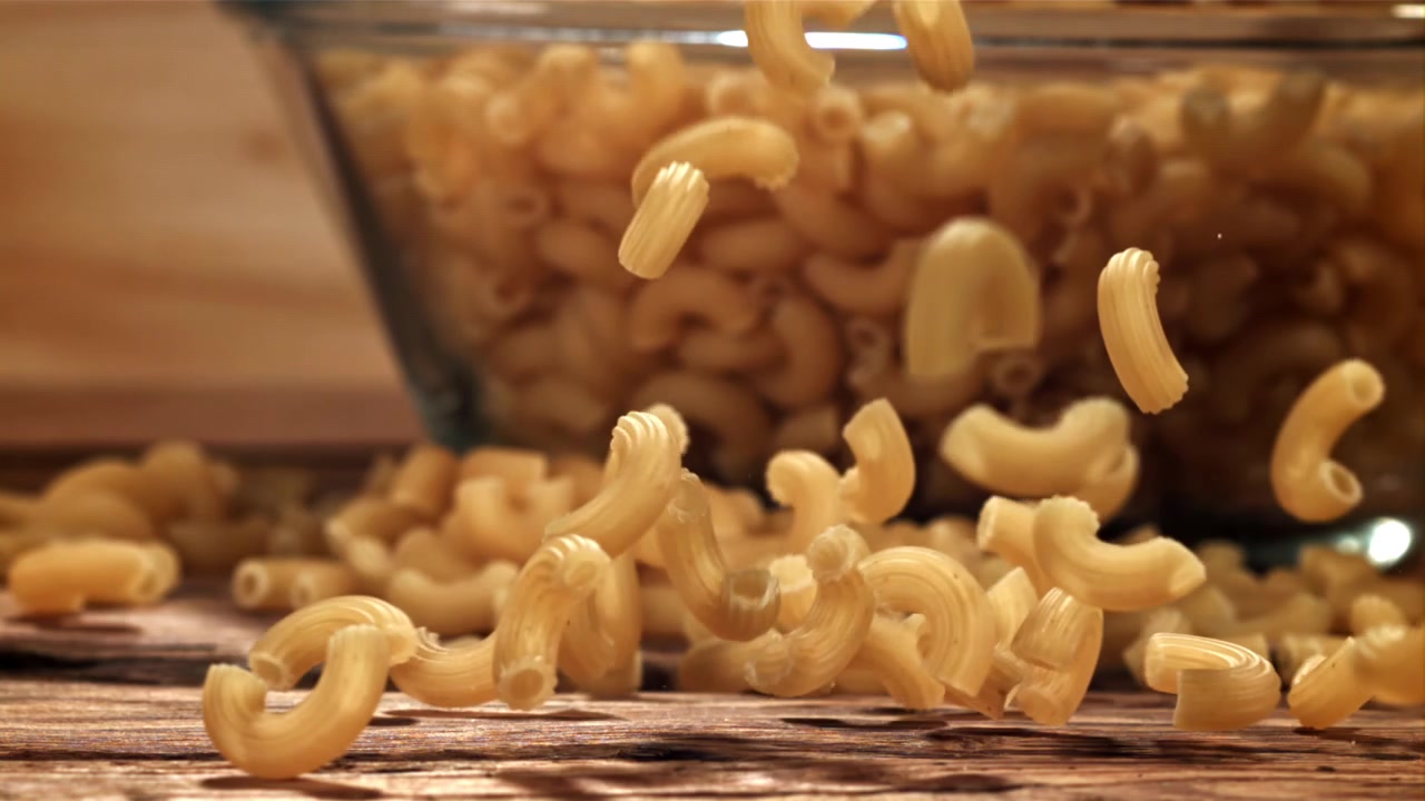 Maccheroni secchi che cadono al rallentatore su un tavolo di legno