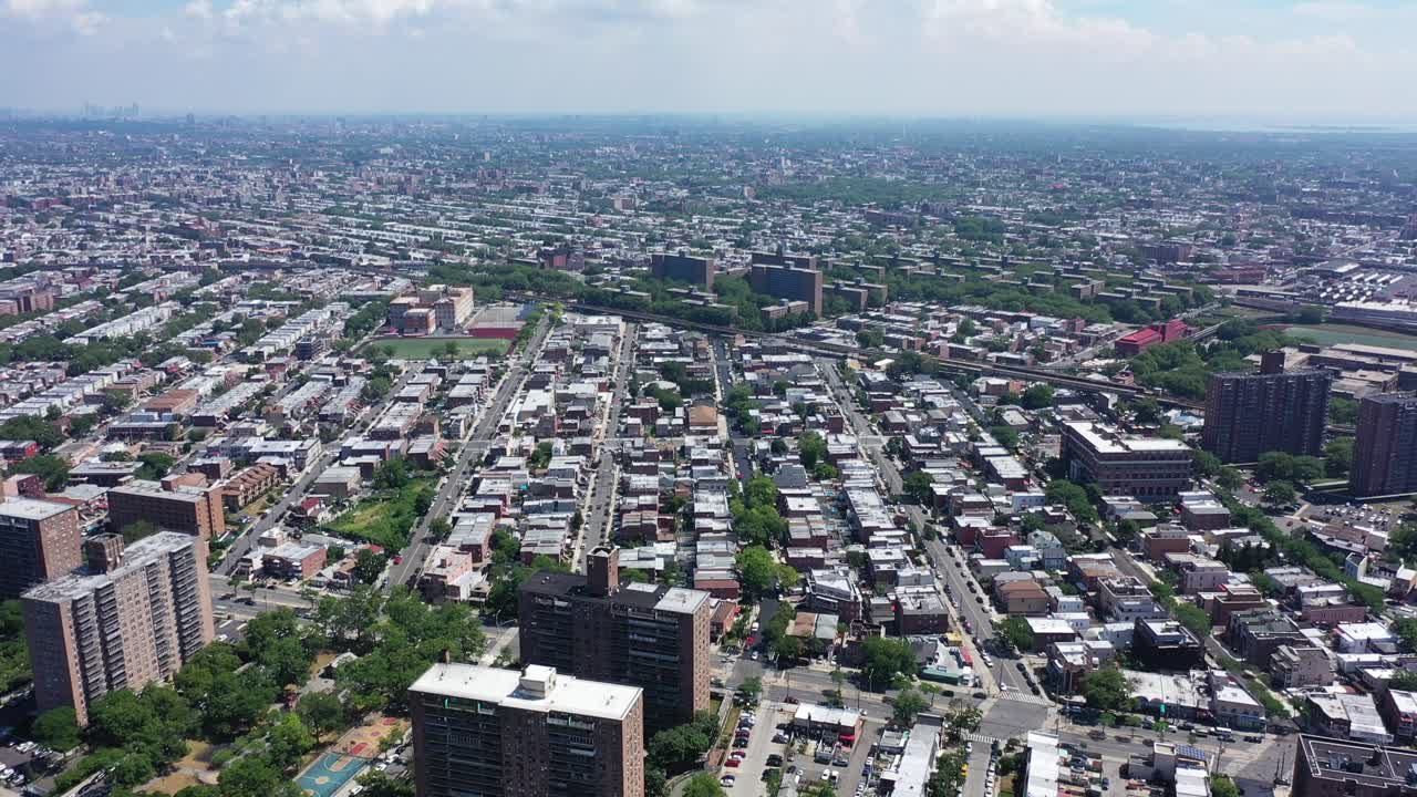 An aerial shot over Brooklyn. The drone hovers high in the sky as the camera tilts up from a ground view of cars driving by on the parkway below. The camera then reveals white clouds and blue skies