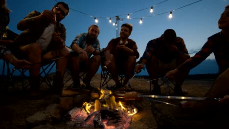 group of traveling friends frying sausages in campsite