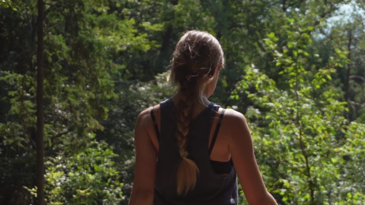 Sporty young woman with long braided hair walking through forest on a sunny day