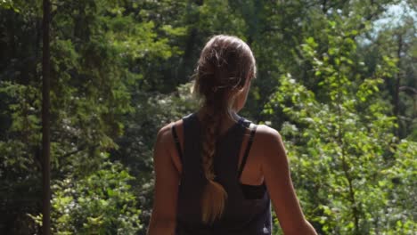 sporty young woman with long braided hair walking through forest on a sunny day