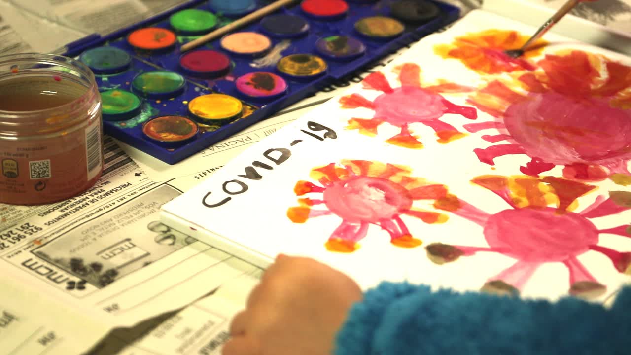 An Artistic Child Painting COVID-19 Corona Virus Illustration on a Drawing Pad With Watercolor And Small Paint Brush - Closeup Shot