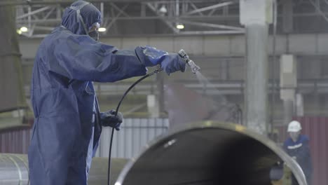 worker applying coating to metal pipe in industrial setting