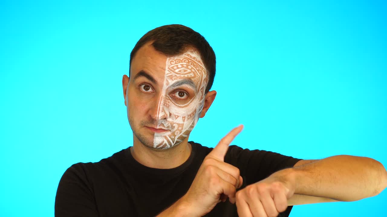 Hombre con la cara pintada se apresura a señalar el reloj, mostrando impaciencia, molesto y enojado por el retraso de la fecha límite