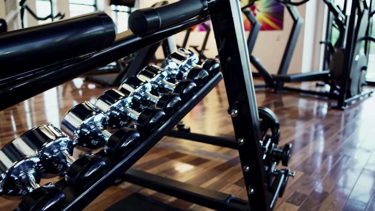 Low-angle video shot of a modern gym with shiny dumbbells on a rack, showcasing sleek design