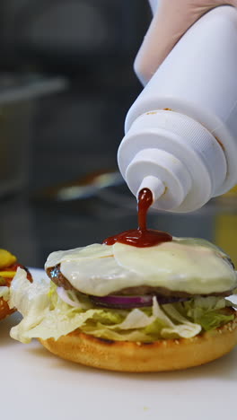 making hamburger in fast food restaurant. hand of man smears sauce on a burger and covers with fried bread. close-up.tasty burgery ready to eat. vertical video