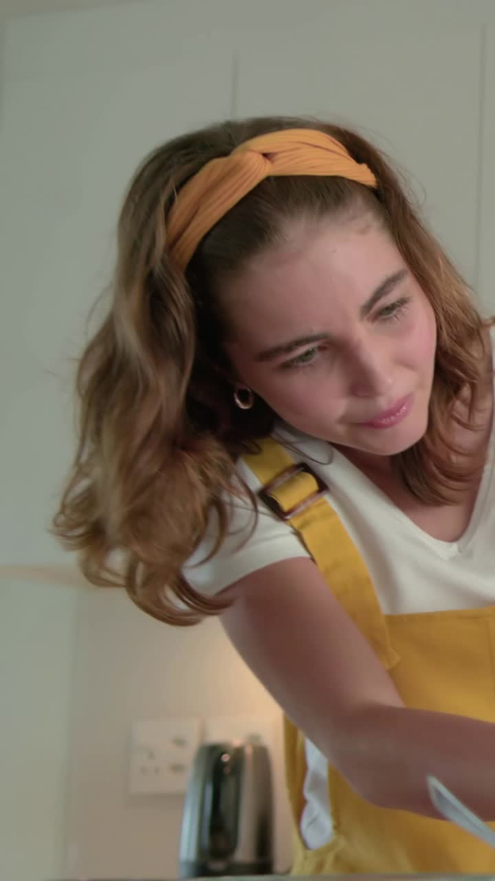 Video vertical: Mujer inclinada con mono amarillo revolviendo un cuenco con una cuchara en la cocina, preparando un aperitivo
