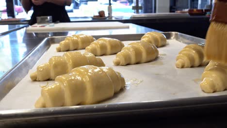 a baker painting egg wash on to croissants that will be baked in a cafe