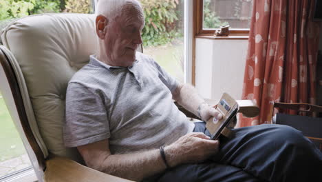 elderly man using a tablet while sitting in an armchair