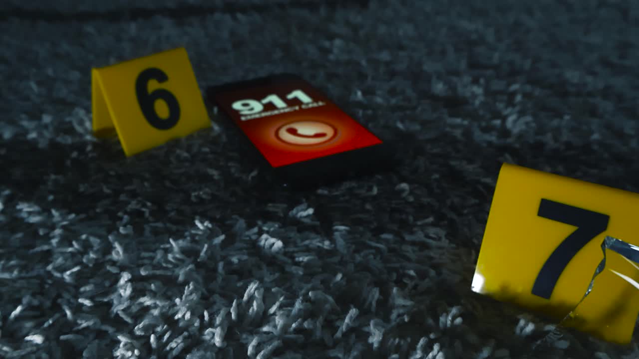 Close up view gliding over yellow police investigation forensic markers placed next to evidence on carpet like a broken wine glass and a phone with a cracked screen calling 911 emergency number