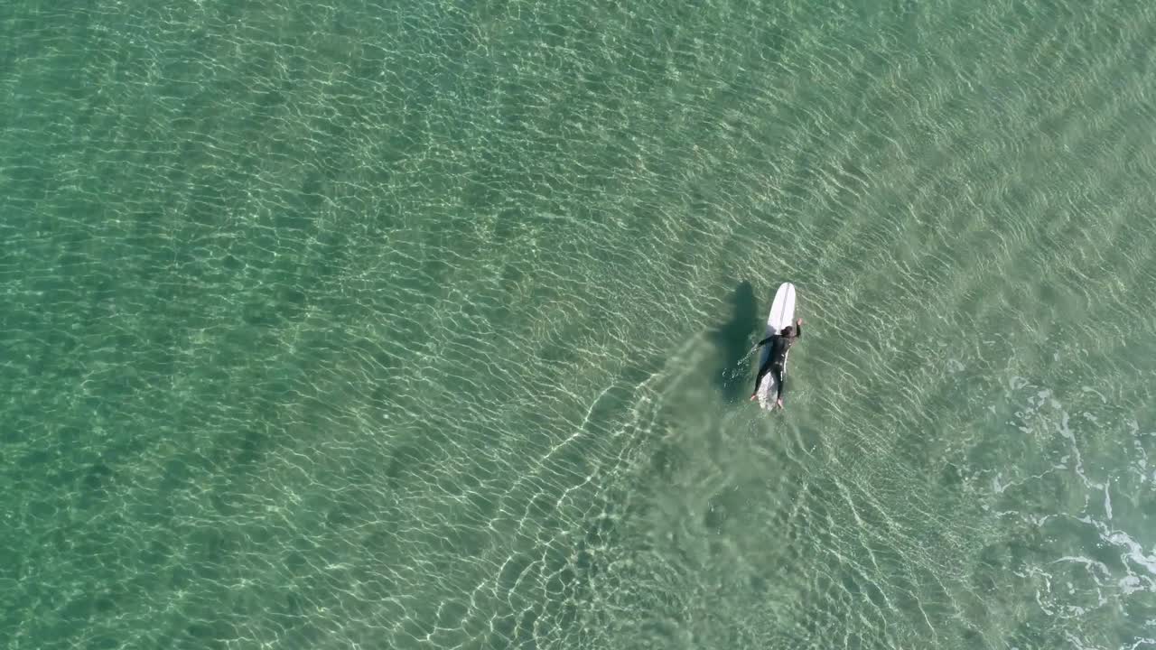 un hombre remando mar adentro en su tabla de surf en aguas claras en un brillante día de verano
