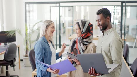 Happy-diverse-business-people-discussing-work-with-laptop-in-office-in-slow-motion