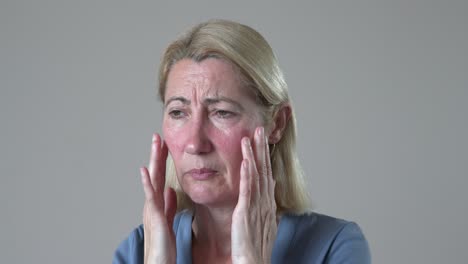 mujer rubia con rosácea en el dolor acariciando la cara roja