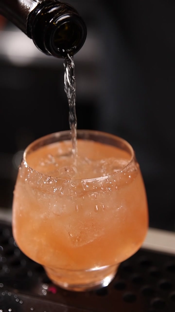 Versare un cocktail rinfrescante all'arancia con ghiaccio in un bicchiere