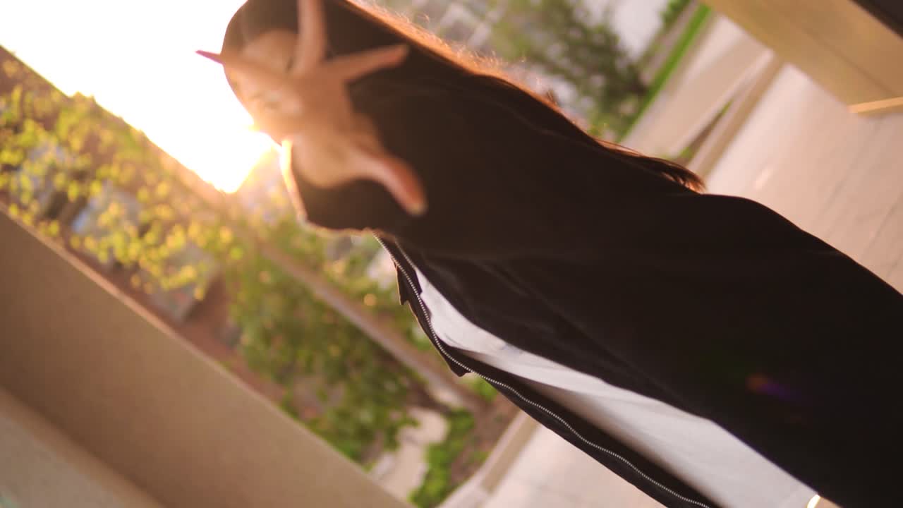 창의적인 스핀 샷 댄서 모델이 카메라를 향해 손을 뻗어 일몰의 황금 시간 설정에서 손으로 호리온을 돌리고 현대적인 패셔너블한 옷을 입은 대도시 공원 슬로우 모션