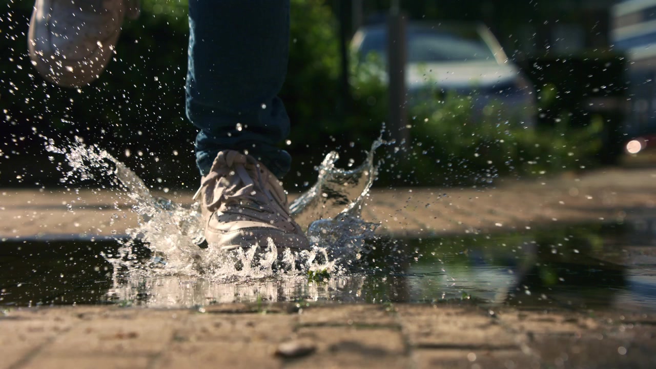 Uomo in jeans e scarpe da ginnastica bianche cammina attraverso una pozzanghera sul marciapiede. Ripreso in super slow motion a 1000fps