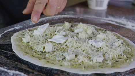 chef añadiendo queso mozzarella y aderezos a la pizza casera en la cocina al aire libre rústica