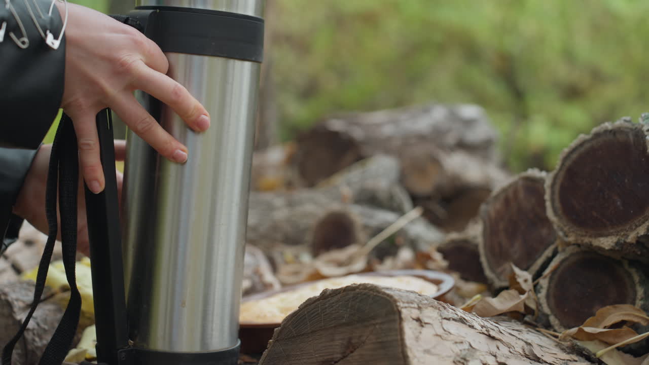 woman in leather jacket placing thermos on log pile in forest, closeup hand setting stainless flask on cut stumps, autumn leaves and moss, rugged bark texture, rock style outfit, urban explorer vibe