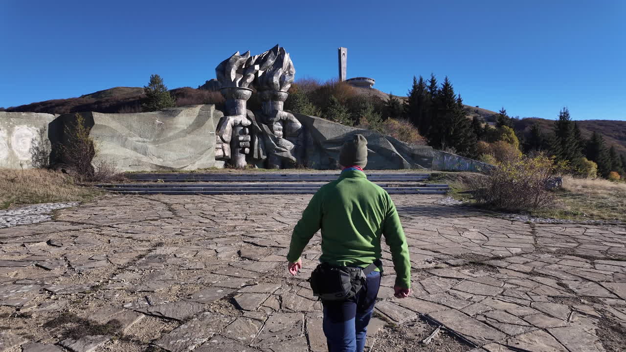 Solitary traveler approaching iconic Buzludzha monument, emblematic communist era structure nestled among Balkan mountain landscape, symbolizing forgotten socialist architectural heritage