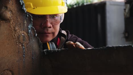 trabajador masculino con gafas de protección y guantes de construcción inspecciona el trabajo después de moler metal con un molinillo angular en el taller doméstico.