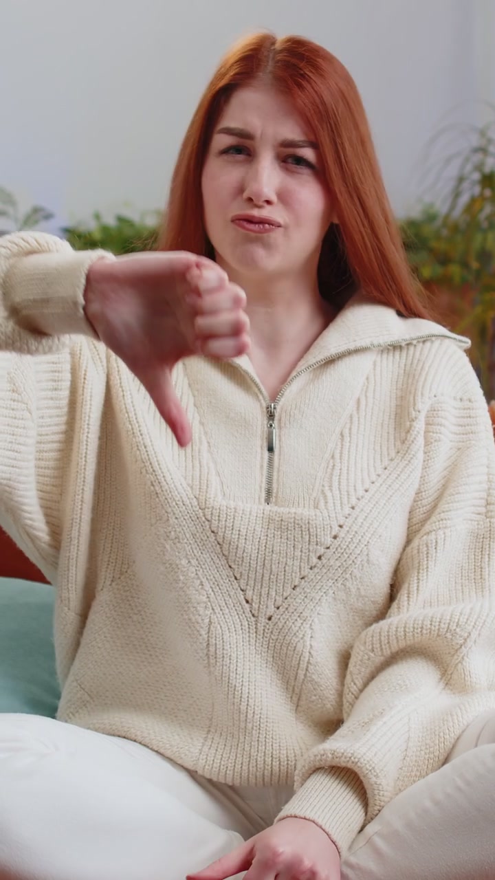 Upset young woman showing thumbs down dislike bad work disapproval dissatisfied feedback at home