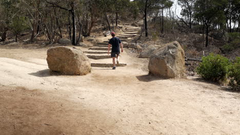 Man-walking-up-to-the-summit-of-the-You-Yangs-National-Park,-Victoria-Australia