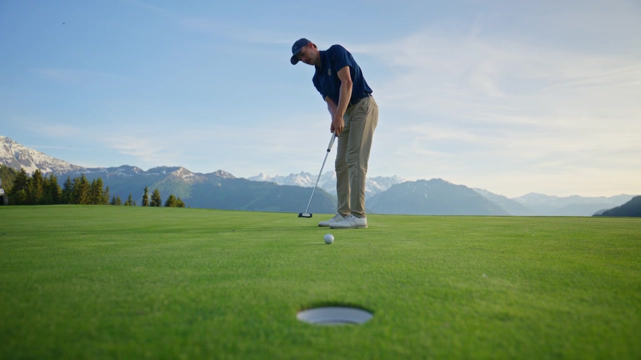 Golfista professionista che si prepara per un putt al Verbier Golf Club in Svizzera. Putt di precisione su un green alpino immacolato con lo spettacolare paesaggio montano delle Alpi svizzere sullo sfondo.