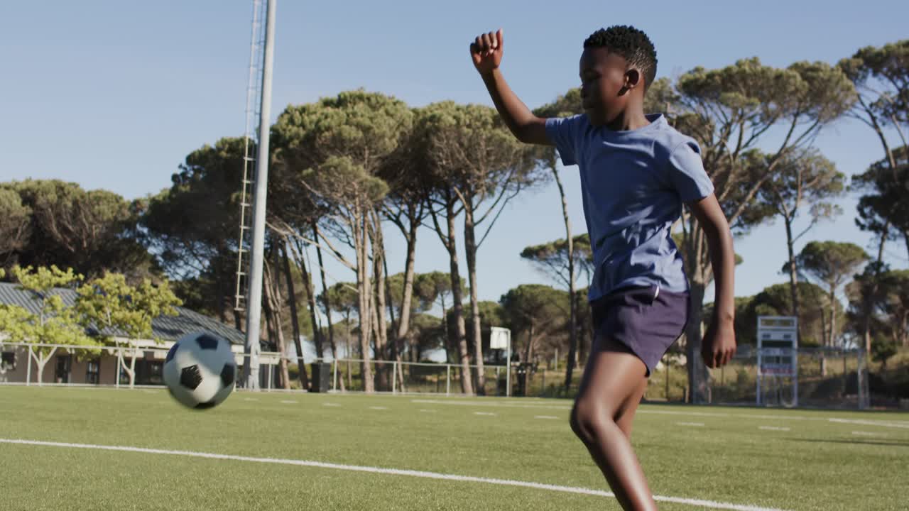 Joven africano con camiseta azul practicando con un balón en los pies, dando toques, haciendo malabares y regateando en una cancha de césped.