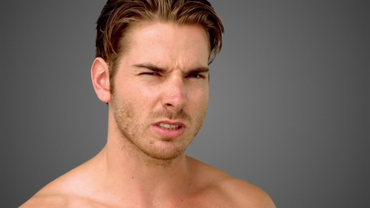 분노 한 남자 가 회색 배경 에 있는 카메라 를 보고 있다